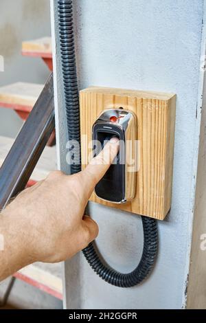 Worker uses contemporary biometric fingerprint scanner to record shift hours worked in workshop of production plant closeup Stock Photo