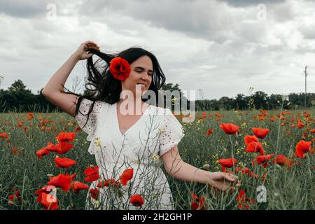 Beautiful young woman wearing white dress, standing in poppy field Stock Photo