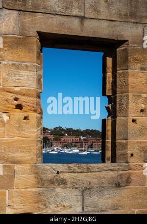 Sandstone brick wall with open window showing boats on water against blue sky Stock Photo
