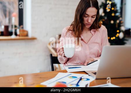 Young woman reading financial report analyzing statistics working at home during winter vacations. Stock Photo