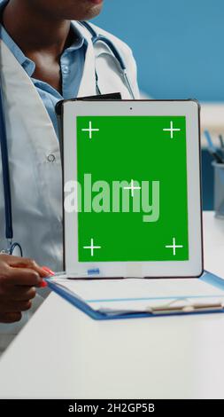 Close up of doctor vertically holding tablet with green screen on desk. Medical specialist showing mockup isolated template and background for chroma key on digital gadget in cabinet Stock Photo