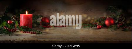 Atmospheric Advent and Christmas decoration with a lit red candle, balls and evergreen yew branches on dark rustic wooden planks, wide panoramic forma Stock Photo