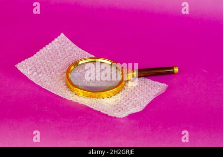 Magnifying glass and bubble wrap on pink background. Selective Focus. Stock Photo