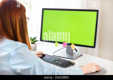 Close up of female hands and PC with green chromakey blank screen. Mock-up of computer monitor. Stock Photo