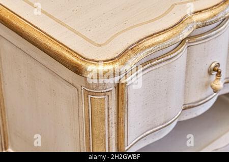 Elegant wooden nightstand made in classical style with drawers with shiny golden decor in light room extreme close view Stock Photo