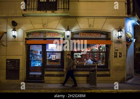 Horizontal night view of a man passing in front of a Pizzeria exterior in Defensa St, San Telmo neighborhood, Buenos Aires, Argentina Stock Photo