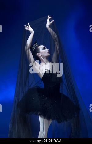 Close-up beautiful ballerina in black tutu and stage make-up posing with black transparent fabric blue studio backgorund Stock Photo