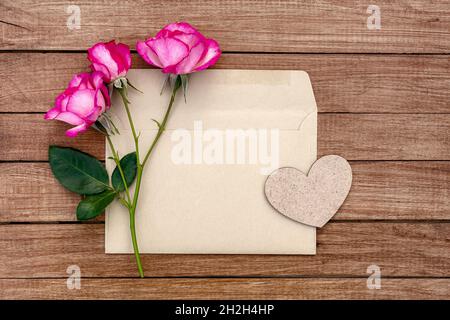 Bouquet of pink roses in an envelope with a heart on a wooden background. Postcard with place for design. Stock Photo