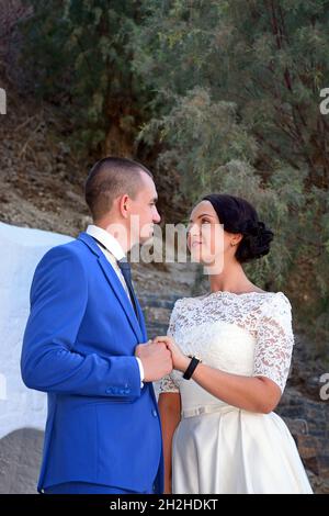 Young bride and groom looking at each other in the port area, Agios Nikolaos, Crete, Greece, Europe. Stock Photo