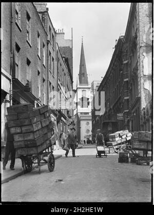 St Mary at Hill, City and County of the City of London, Greater London Authority, 1930s. A view looking north along St Mary at Hill towards St Margaret Pattens Church on Rood Lane, showing handcarts in the foreground loaded with crates. With its close proximity to the River Thames and the old Billingsgate Fish Market, the buildings on St Mary at Hill were occupied by a number of fish salesmen. Stock Photo