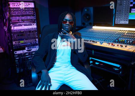 Portrait of African young man in sunglasses sitting in the music studio with musical keyboard in the background Stock Photo