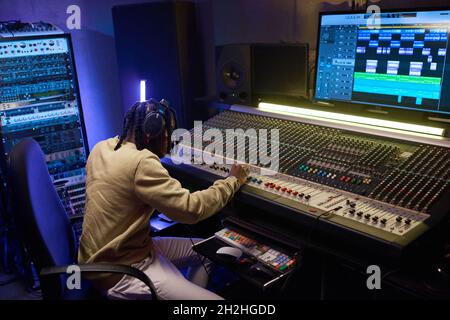 African musical producer in headphones working on sound mixing board in digital recording studio Stock Photo