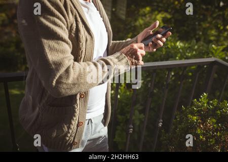 Senior caucasian man using smartphone at balcony on sunny day Stock Photo