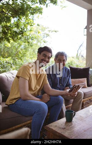 Portrait of smiling biracial adult son and senior father using tablet Stock Photo