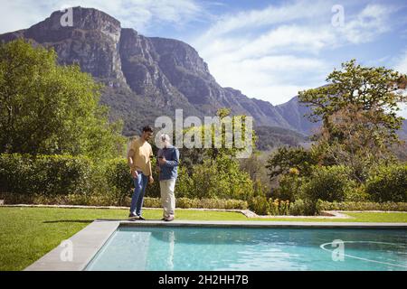 Smiling biracial adult son and senior father using smartphone in garden Stock Photo