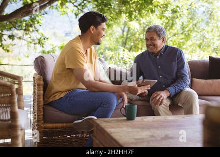 Smiling biracial adult son and senior father using tablet in garden Stock Photo