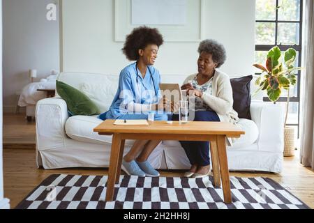 Smiling african american female doctor using tablet with senior female patient at home Stock Photo
