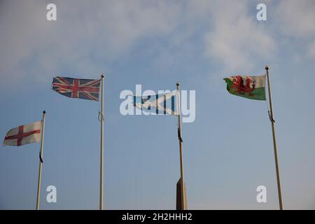 National flags of the UK, Scotland, England and Wales seen flying on flagpoles in a strong wind. Stock Photo