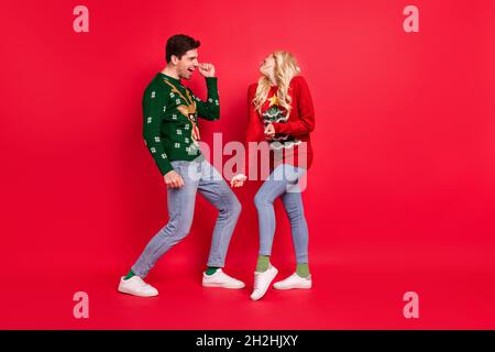 Full length body size photo dancing people laughing in ugly jumpers isolated vivid red color background Stock Photo