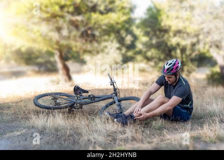 Male cyclist in an accident in the countryside. A young cyclist lying on the ground after suffering a fall from his bicycle in which he injured his an Stock Photo