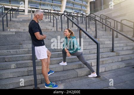 Healthy mature couple chatting while standing outdoors after morning workout in the city Stock Photo
