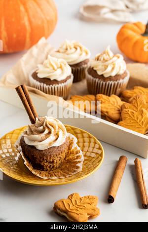 A tray of pumpkin spice cupcakes and cookies with a cupcake on a plate in front. Stock Photo