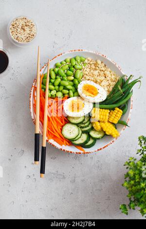 Healthy salad with couscous, carrots, cucumber, green beans, soybeans, corn and an egg on a gray concrete background. Food and health. Buddha bowl sal Stock Photo