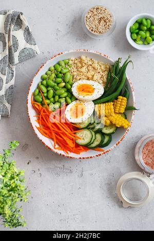 Healthy salad with couscous, carrots, cucumber, green beans, soybeans, corn and an egg on a gray concrete background. Food and health. Buddha bowl sal Stock Photo