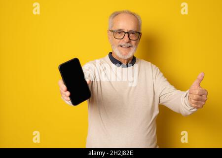 Lifestyle, tehnology and old people concept: Handsome old gray-haired man dressed in smart casual style using a smartphone and smiling over yellow bac Stock Photo