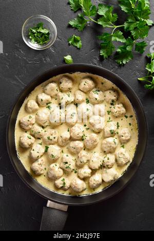 Swedish style meatballs with creamy white sauce in frying pan over black stone background. Top view, flat lay, close up Stock Photo