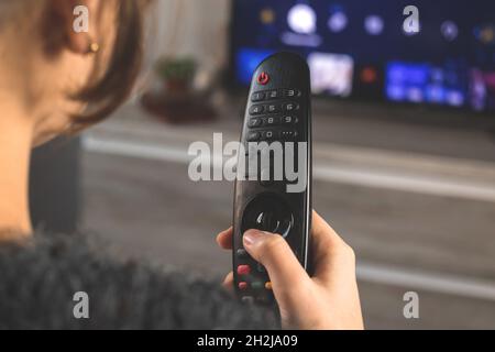 Woman sitting on sofa with TV remote control in front of TV and watch streaming services concept Stock Photo