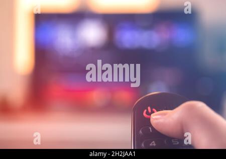 Hand with TV remote control turn off the television by pressing on red button, selective focus Stock Photo