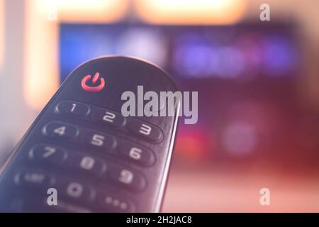 Remote smart TV control close-up on a background with television, selective focus, copy space, neon lights Stock Photo