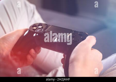 Female hands holding gaming controller. Concept of modern streaming and gaming with big tv sitting at home on sofa, leisure Stock Photo
