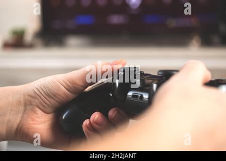 Hands holding gaming controller and playing game on a tv. Concept of modern streaming sitting at home on sofa, leisure Stock Photo