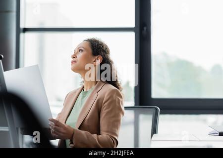 african american businesswoman holding document and looking away while thinking in office Stock Photo