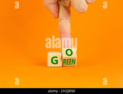 Ecology and go green symbol. Businessman turns a wooden cube with concept words 'Go green' on a beautiful orange table, orange background. Copy space. Stock Photo