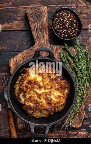 Fried Potato pancakes or Fritters with herbs in a pan. Dark wooden background. Top view Stock Photo