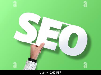 hand holding SEO sign against green background, search engine optimization concept Stock Photo