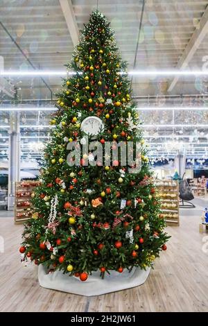 Christmas tree decorated with clocks, colorful toys, garlands and lights in the store for the winter holidays Blurred background with sequins garlands Stock Photo