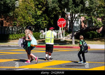 School children crossing a busy street with the aid of a crossing guard Stock Photo