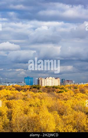dark gray rainy clouds in blue sky over lush yellow forest and modern high-rise apartment houses illuminated by sun on autumn day before rain Stock Photo