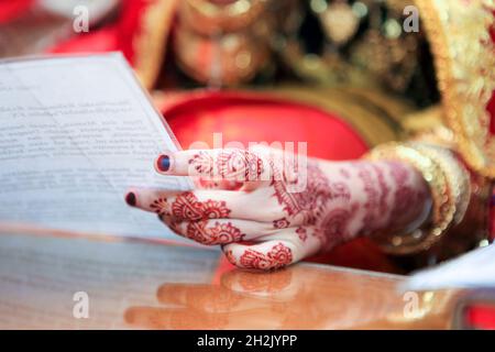 Close up of hand and nails of Asian Muslim bride with henna tattoo and jewelry holding paper contains prayer in Minangkabau culture wedding ceremony