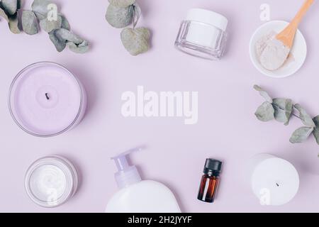 Flat lay composition with natural cosmetics for face and body, moisturizer cream, clay and essential oil next to candles and eucalyptus leaves on lila Stock Photo