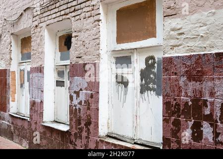 facade of old shabby brick house tiled with soiled tiles with poorly painted over white paint windows Stock Photo
