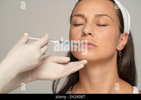 Portrait of a young satisfied woman on a lip filler injection procedure on gray background Stock Photo