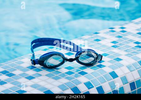 Blue professional swimming goggles with water drops on yellow lenses on a blue and white tiles of pool floor. Stock Photo