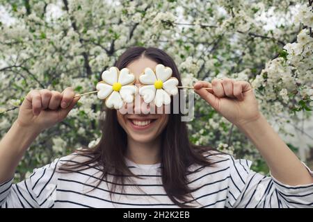 Smiling girl hide eyes with gingerbread pastry on sticks in daisy flower shape Stock Photo