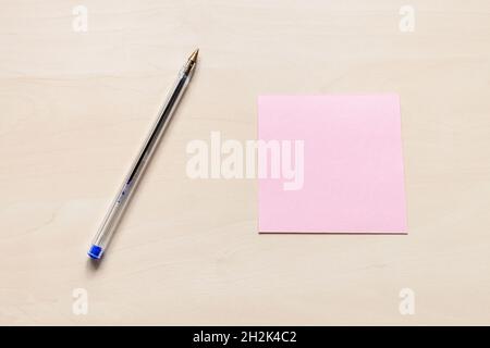 top view of blank pink sheet of note paper and blue pen on light brown wooden board Stock Photo