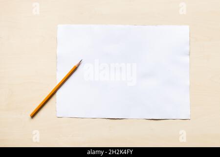 top view of regular pencil on blank sheet of white textured watercolour paper on light brown wooden board Stock Photo
